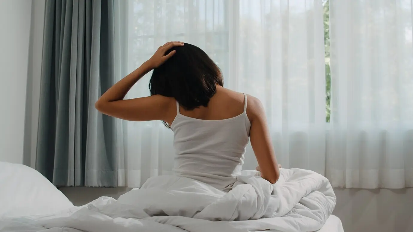A teenage Hispanic woman wakes up at home. A young Asian girl stretches on her bed near the bedroom window in the morning after sleeping all night, starting a new day with energy and vitality and feeling very refreshed.
